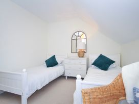 A bedroom with two single beds a white chest of drawers with a lamp and mirror and a wicker chair at Lowenna Manor 3 Rock