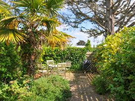 An outdoor patio area with a table and four chairs surrounded by green plants and trees at Lowenna Manor 3 in Rock