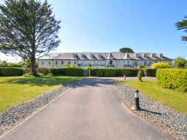A driveway leading to a long building with multiple windows and turrets surrounded by grass and trees at Lowenna Manor 3 in Rock
