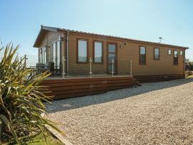 A wooden lodge with windows and decking in an outdoor area at Sunstone Lodge (Garreg Haul Lodge) Cilan near Abersoch