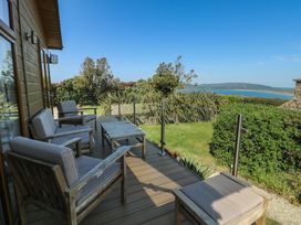 A deck area with wooden chairs and a table at Sunstone Lodge (Garreg Haul Lodge) Cilan near Abersoch