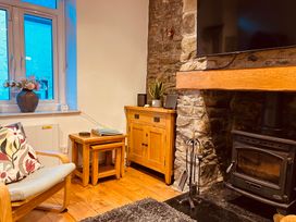 A corner of a living room with a wooden chair with a floral cushion a set of nest tables a wooden cabinet stone fireplace with a wood stove and a mounted television at 7 Watkin Street in Conwy