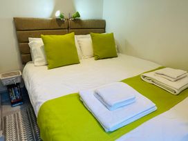 A bedroom with a bed with white sheets green pillows and folded towels at 7 Watkin Street in Conwy
