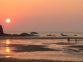 A beach scene with a sunset and people on the sand at Porthcothan House in Porthcothan