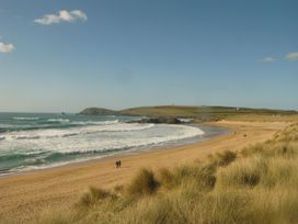 A beach with waves and people walking at Porthcothan House in Porthcothan