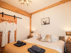 A bedroom with a bed covered in a yellow blanket and pillows with a rabbit design two bedside tables with lamps wooden beams on the ceiling and two white robes hanging on a wooden door at Pine Marten Lodge in Dulnain Bridge near Nethy Bridge