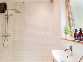 A bathroom with a shower area with white tiled walls a sink a window with toiletries and a small plant on the ledge at Pine Marten Lodge in Dulnain Bridge near Nethy Bridge