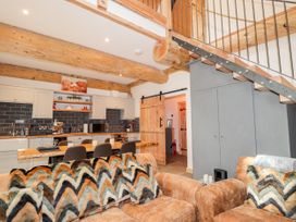 An open-plan kitchen and living area with wooden beams a staircase and patterned cushions on sofas at Pine Marten Lodge in Dulnain Bridge near Nethy Bridge