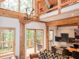A kitchen and dining area with wooden beams and large windows showing trees at Pine Marten Lodge in Dulnain Bridge near Nethy Bridge
