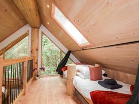 A bedroom with wooden walls and ceiling two single beds with pillows and blankets and large triangular window overlooking trees at Pine Marten Lodge in Dulnain Bridge near Nethy Bridge