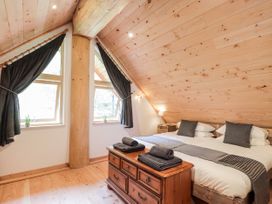 A bedroom with a double bed wooden chest black curtains and slanted wooden ceiling at Pine Marten Lodge Dulnain Bridge near Nethy Bridge