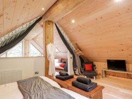 An attic bedroom with a bed towels on a wooden chest a chair with a red cushion and a television on a bench at Pine Marten Lodge Dulnain Bridge near Nethy Bridge
