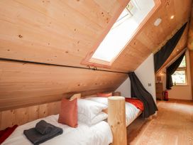 A bedroom with a wooden bed under a slanted wooden ceiling with a skylight and a window with dark curtains at Pine Marten Lodge in Dulnain Bridge near Nethy Bridge