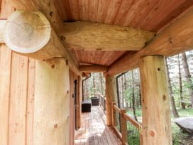 A wooden porch with large log pillars and outdoor furniture surrounded by trees at Pine Marten Lodge in Dulnain Bridge near Nethy Bridge