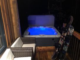 A hot tub with blue lights on a wooden deck with snowy sport equipment and wicker chairs at Pine Marten Lodge in Dulnain Bridge near Nethy Bridge
