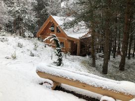 A wooden cabin in a snowy forest with a log bench covered in snow at Pine Marten Lodge Dulnain Bridge near Nethy Bridge