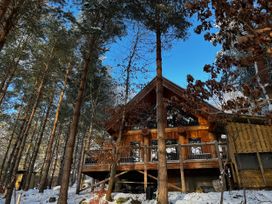 A wooden cabin with a deck among snow-covered trees under a blue sky at Pine Marten Lodge in Dulnain Bridge near Nethy Bridge