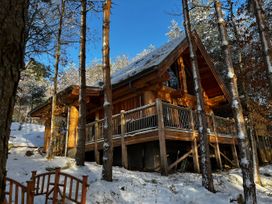 A wooden cabin surrounded by snow-covered trees with a wooden gate in front at Pine Marten Lodge in Dulnain Bridge near Nethy Bridge