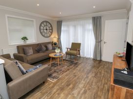 A living room with sofas a chair a coffee table and a wall clock at Rookley Lake Cottage in Rookley near Godshill