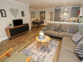 An open living room and kitchen area with sofas, a coffee table on a rug, a TV on a wooden cabinet, and a dining table with chairs at Rookley Lake Cottage in Rookley near Godshill