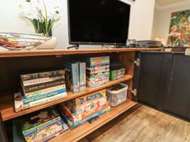 A wooden cabinet with a television on top and shelves inside containing books board games DVDs and a game controller at Rookley Lake Cottage in Rookley near Godshill