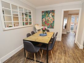 A dining area with a wooden table and six grey chairs a floral wall art and large mirror on the wall at Rookley Lake Cottage in Rookley near Godshill
