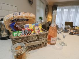 A kitchen countertop with a wicker basket containing breakfast items a loaf of bread a bottle of rose wine and two wine glasses at Rookley Lake Cottage in Rookley near Godshill