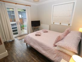 A bedroom with a double bed with pink polka dot bedding a small TV on a wooden stand next to glass doors and a window with a striped blind at Rookley Lake Cottage in Rookley near Godshill