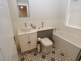 A bathroom with a white sink cabinet a toilet a bathtub and patterned floor tiles at Rookley Lake Cottage in Rookley near Godshill