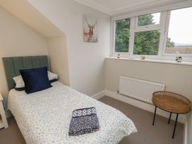 A bedroom with a single bed, a window with a view of trees, a round wicker side table, and a painting of a deer on the wall at Rookley Lake Cottage in Rookley near Godshill