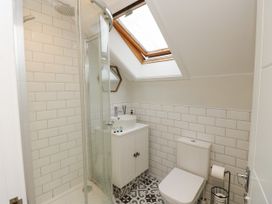 A bathroom with a glass shower enclosure a white toilet a white sink cabinet a hexagonal mirror and a skylight window at Rookley Lake Cottage in Rookley near Godshill