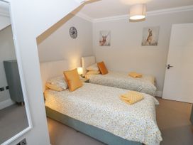 A bedroom with two single beds side by side with floral bedding and orange cushions a bedside table with a lamp wall art of a deer and a hare a clock and a mirror at Rookley Lake Cottage in Rookley near Godshill