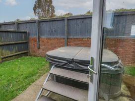 A hot tub with steps in a backyard with a grass lawn and wooden fence at Rookley Lake Cottage in Rookley near Godshill
