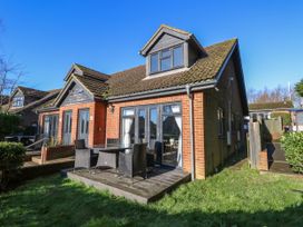 A brick house with a wooden deck and outdoor dining set in a grassy yard at Rookley Lake Cottage in Rookley near Godshill