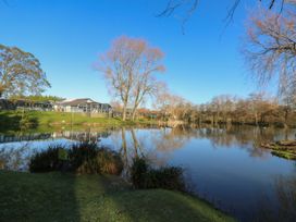 A lake with surrounding trees and a building on the left under a clear sky at Rookley Lake Cottage in Rookley near Godshill