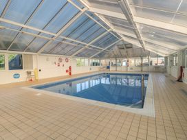 An indoor swimming pool with tiled floor and metal handrails inside a glass roof enclosure at Rookley Lake Cottage in Rookley near Godshill