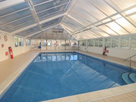 An indoor swimming pool with tiled floor windows and tables at Rookley Lake Cottage in Rookley near Godshill