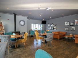 A lounge area with tables and upholstered chairs a wood stove and framed pictures on the walls at Rookley Lake Cottage in Rookley near Godshill