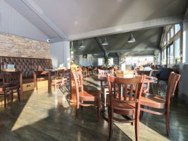 A dining area with wooden chairs and tables and a long cushioned bench along a brick wall at Rookley Lake Cottage in Rookley near Godshill