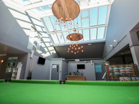 A room with a green pool table under a glass ceiling with hanging lights and gray walls with signs at Rookley Lake Cottage in Rookley near Godshill