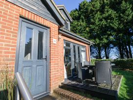An outdoor patio area with a table and four chairs next to a brick house with blue doors and windows at Rookley Lake Cottage in Rookley near Godshill