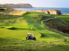 A golf course with a cart on the green and cliffs overlooking the ocean at The Captain's Nest in Bunbeg, County Donegal