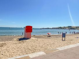 A beach with a striped beach hut and people enjoying the water at The Barn in Lytchett Matravers