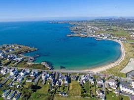 An aerial view of a coastal village with houses along a curved shoreline and blue sea at Moorside in Trearddur Bay