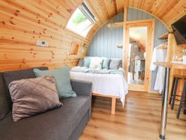 A wooden pod interior with a grey sofa and a bed with pillows at Mallard View in Cockerham near Lancaster
