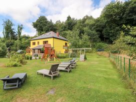 A garden with a yellow house, swing set, and deck chairs at The Woodlands Lower Level in Stepaside