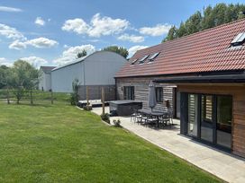 A patio with outdoor dining furniture and hot tub next to a lawn and wooden house at The Gully in Sherborne