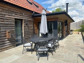 An outdoor patio with a metal dining table and six chairs an umbrella against a wooden house at The Gully in Sherborne