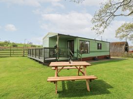 A green mobile home with a wooden deck and picnic table on a grassy lawn with trees and a barn at Row End farm in Brough