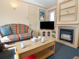 A living room with a checkered sofa a wooden coffee table with teapot and mugs a television and a fireplace at Row End farm in Brough